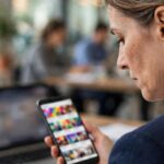Brand manager reviewing low-quality AI-generated social media posts on her phone in an office, seen from behind